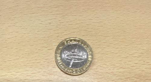A 2016 British pound coin commerative of William Shakespear  resting on a light-colored wooden surface.