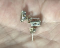 A pair of small silver-stud earrings with rectangular clear stones and a central star detail, resting on an open palm.