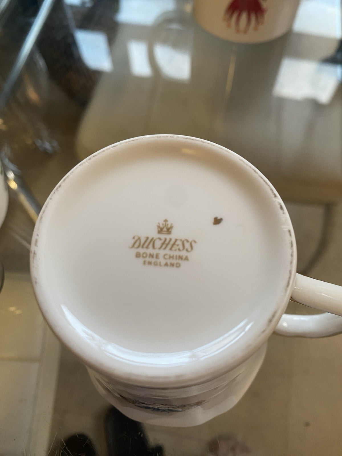 The underside of the white ceramic mug shown from the bottom, featuring the gold printed brand name 'Duchess Bone China England' on the inside of the rim.