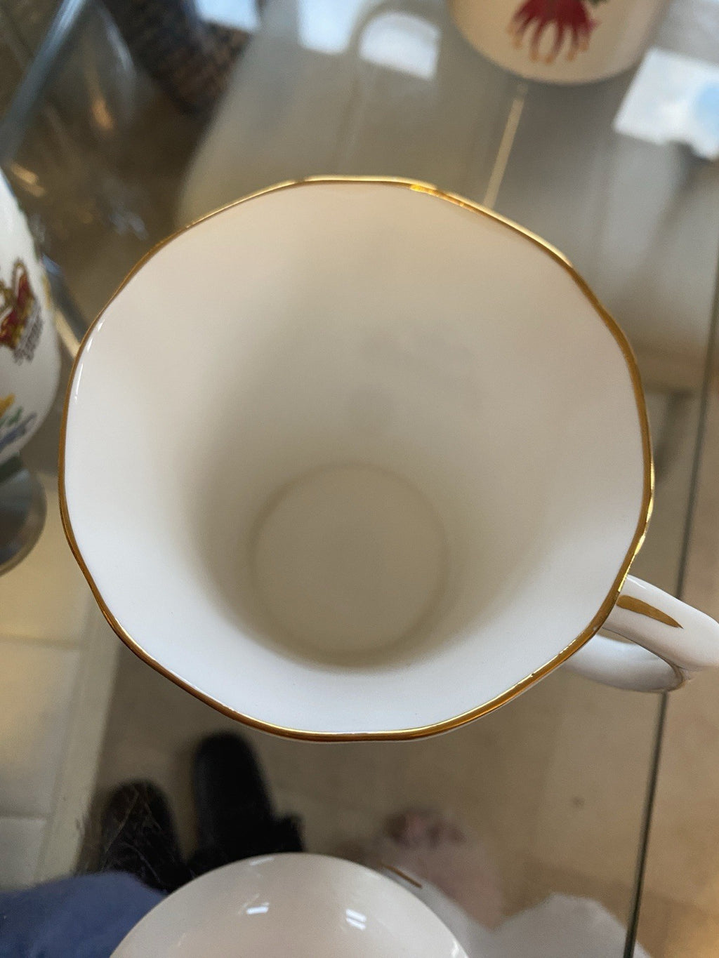 A white porcelain tea mug viewed from above, featuring a thin gold rim and a white handle, resting on a glass table.
Small signs of wear commensurate with age