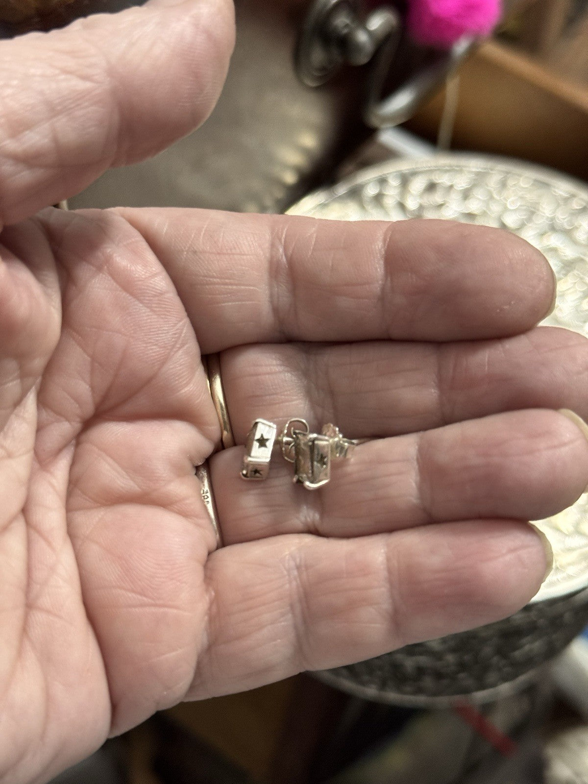 A close-up of a person's hand holding a pair of small Silver Earrings with stars in the bezels, A blurred background.