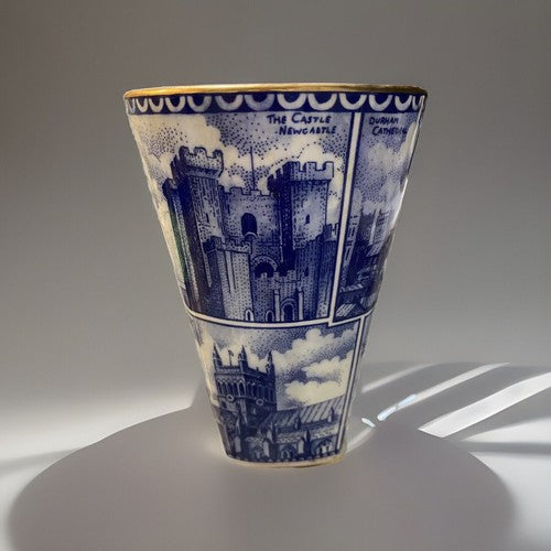 A blue and white illustrated ceramic Vase, Ringtons Tea Collectibles, Landmark Vase with blue architectural cityscape panels and gold trim, photographed on a light gray studio background with a cast shadow.