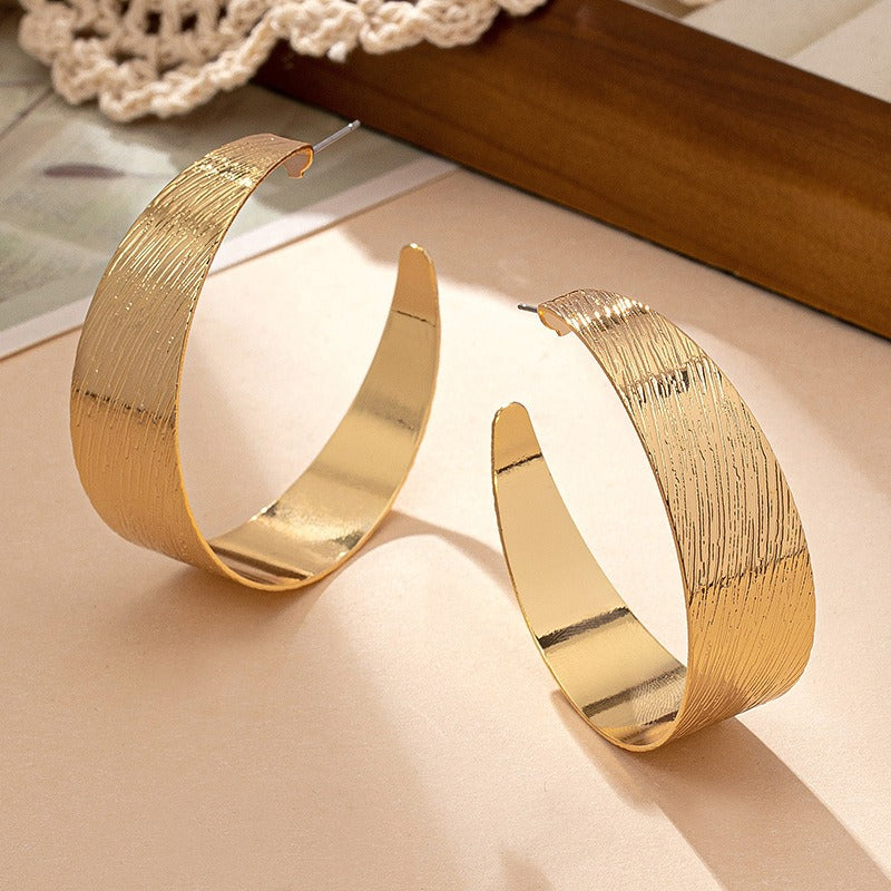 An Alternative view of the textured earrings in a half hoop style with a post and stud. Very 80's. On a cream background with other items in the backround