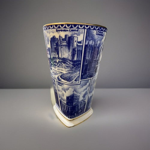 A blue and white illustrated Vase. One of The Ringtons Collectibles with a gold rim, featuring scenic architectural panels, displayed on a white stand against a gray background. Its a square design Vase with many famous Landarks from the United Kingdom of Great Britain