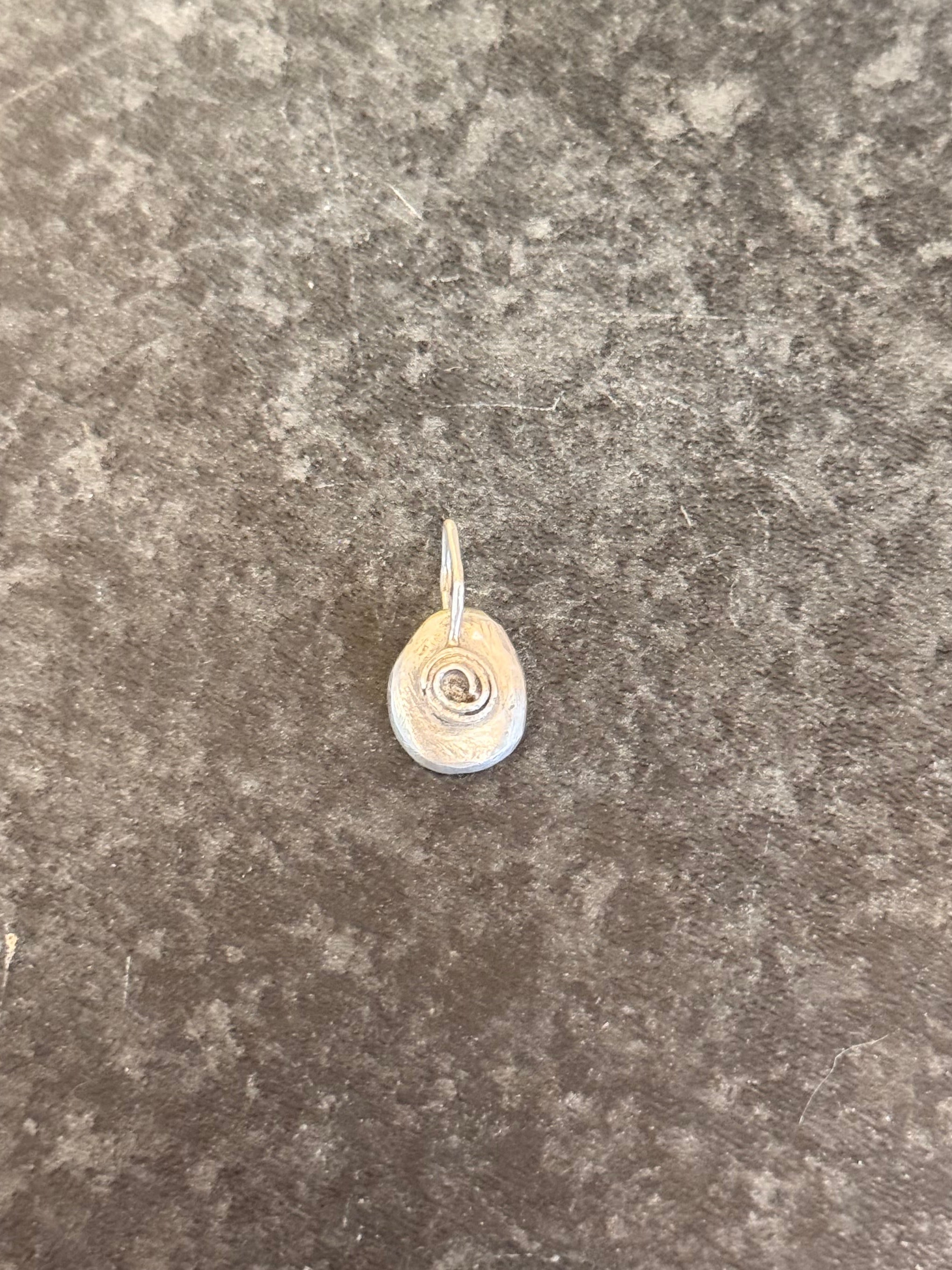 A small silver oval pendant with a rose design in the center, resting on a textured gray stone surface.