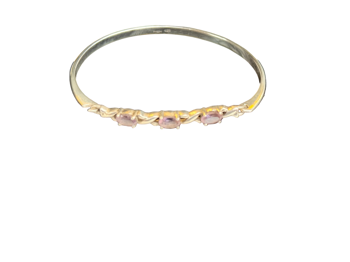 A Sterling Silver Hallmarked bangle bracelet featuring three small, oval-cut light pink gemstones set along the front band, photographed against a solid white background.