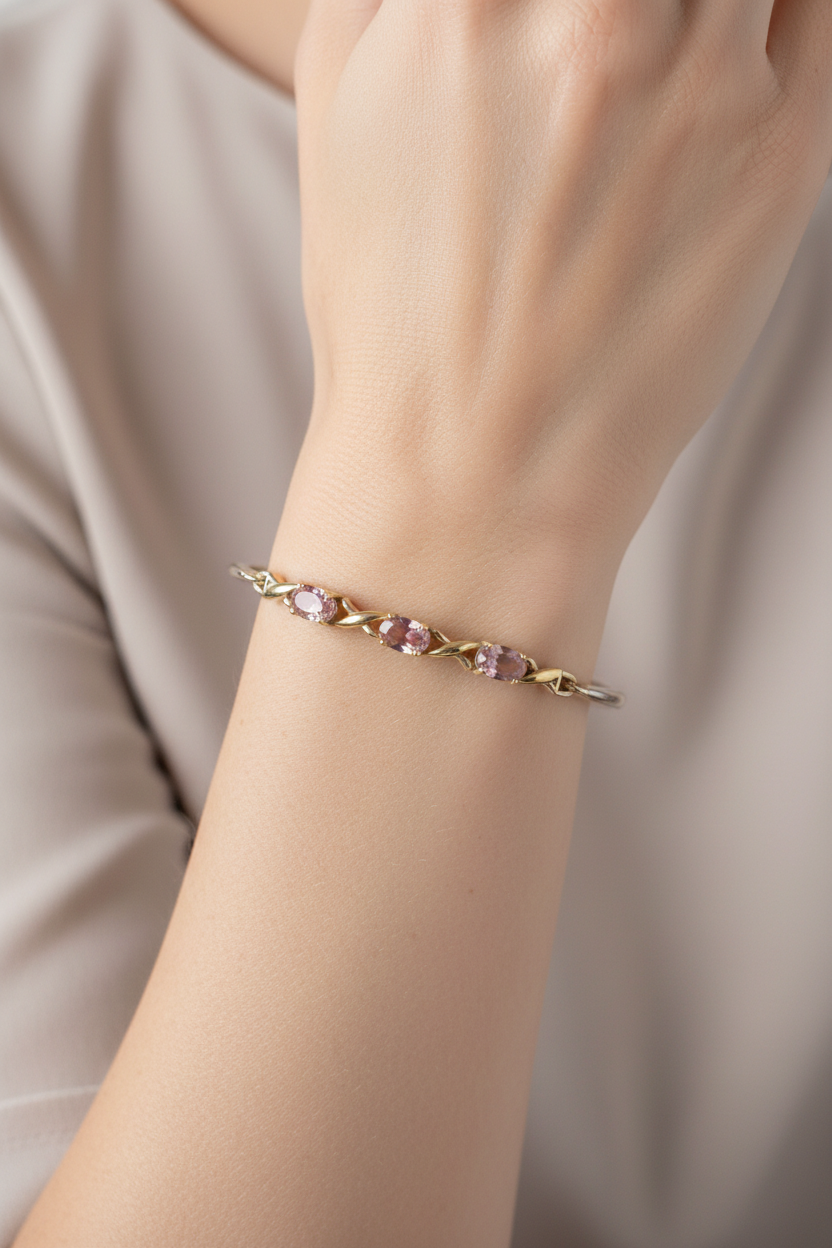 A delicate gold bracelet with three oval pink/purple toned gemstones, worn on a person's wrist against a soft beige top.
This image is an Ai image to show how its looks on a person