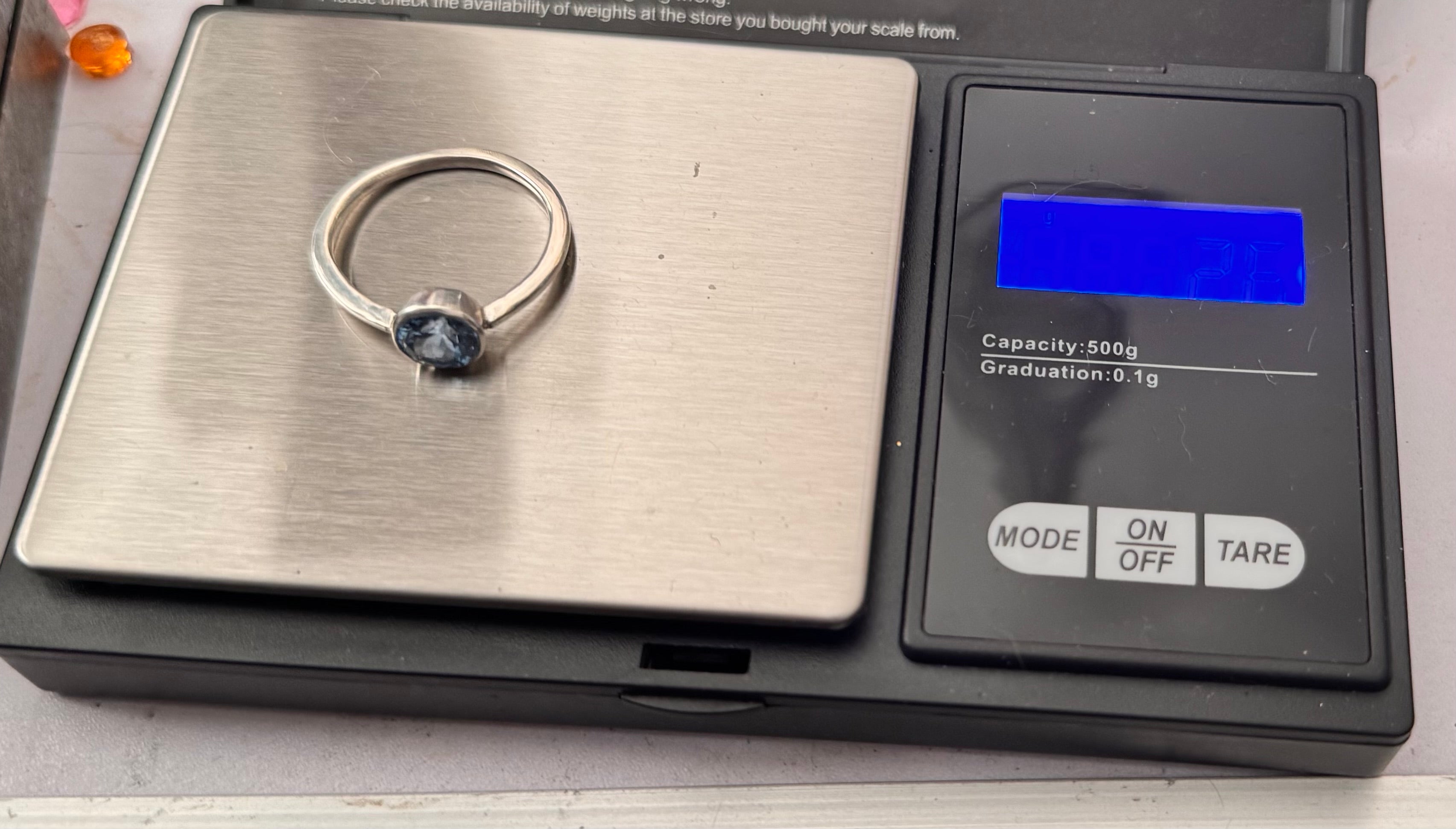 A sterling silver ring with a round dark blue gemstone is shown on a digital scale displaying 2.8g. not very visible but thats the weight