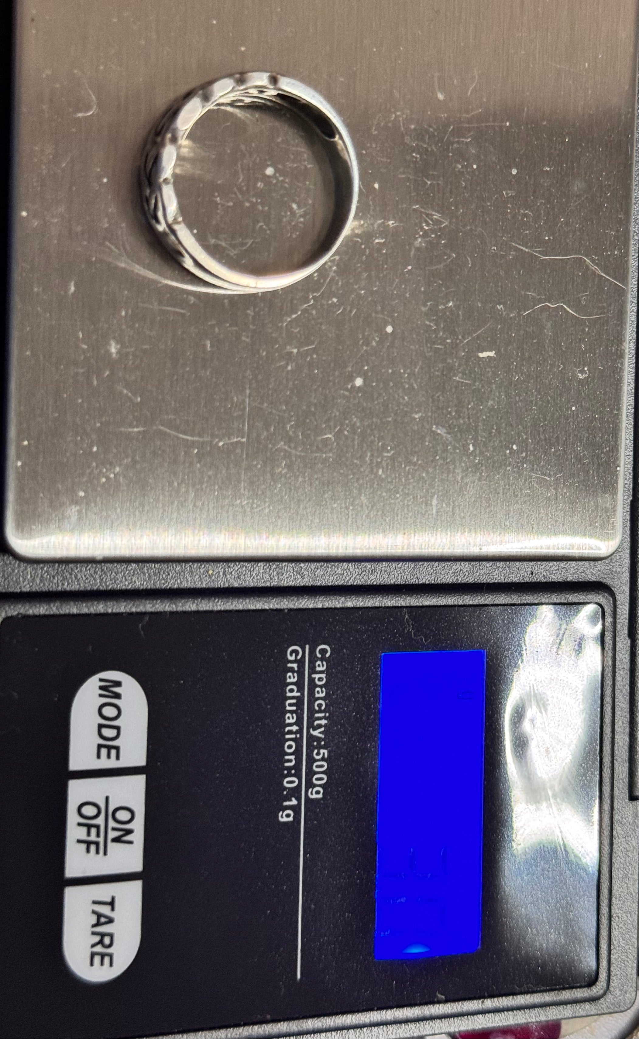 The sterling silver Celtic ring  is shown resting on the metal weighing platform of a digital scale. The scale display is not very visible but it does state 3 grams