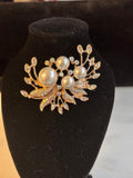A gold-toned brooch featuring faux pearls and rhinestone-embellished leaves, displayed on a black velvet jewelry bust.