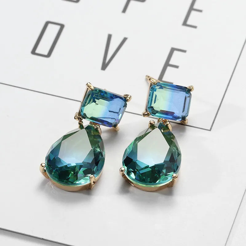 This image displays the drop earrings laid on white surface with the word LOVE in the background