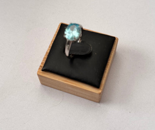 A silver ring with a round light blue gemstone displayed on a small wooden jewelry box with a black cushion, set against a plain light gray background. Aquamarine Sterling Silver Adjustable Ring Size N½ Halmarked