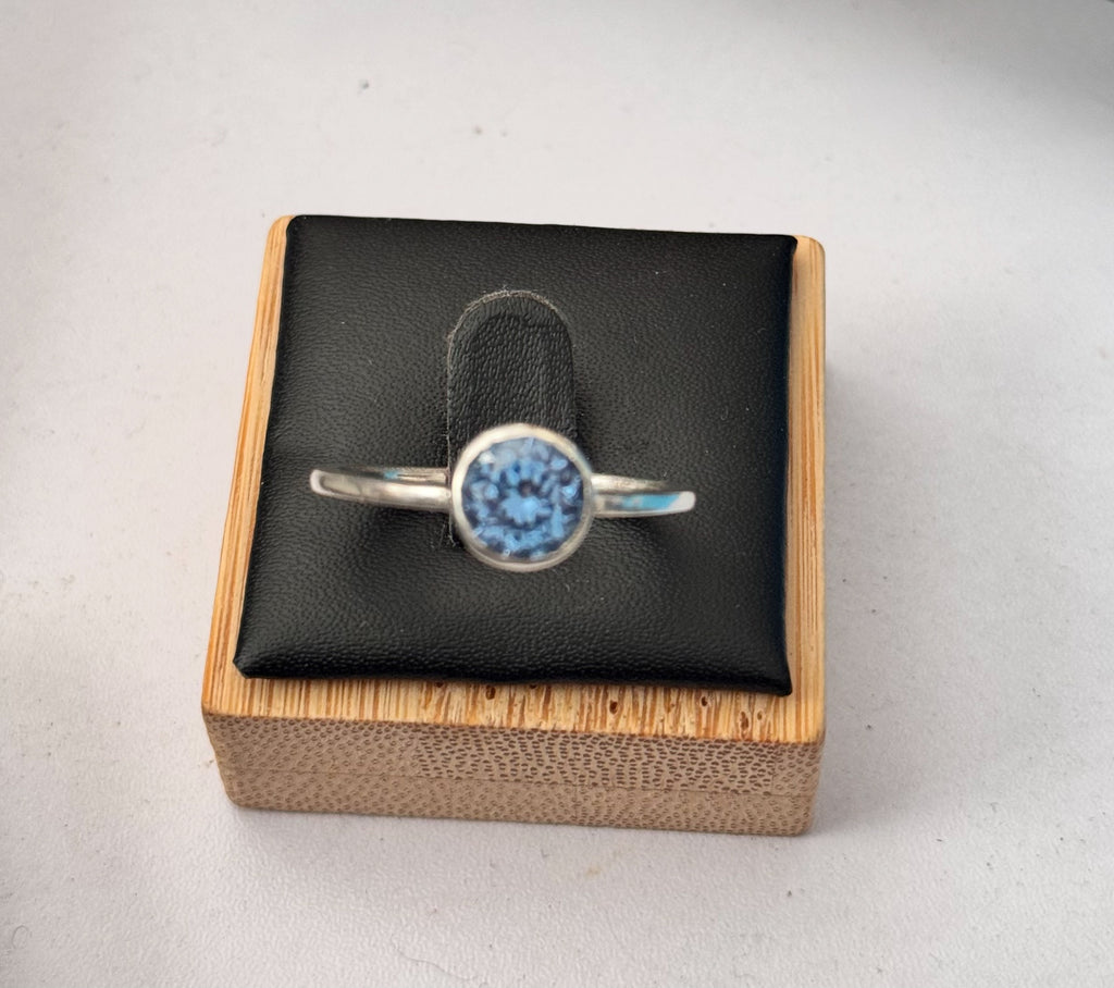 A sterling silver ring with an uncertificated lab sapphire a round gemstone, displayed on a black cushion inside a wooden box.