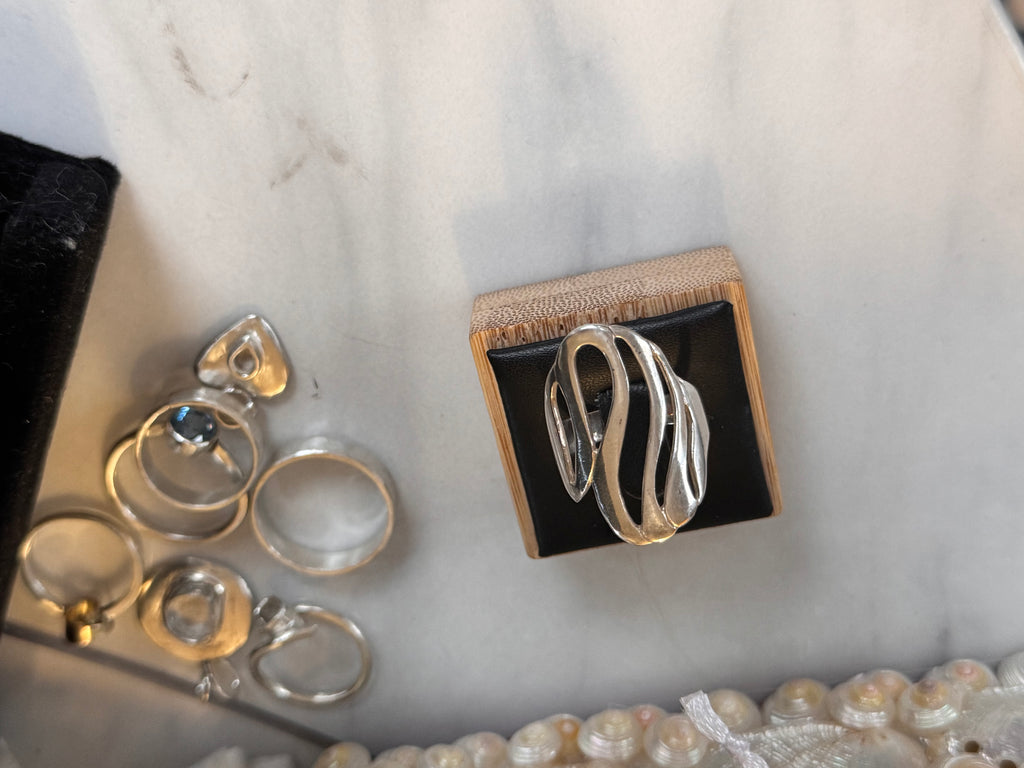 Sterling Silver Wave Design Ring on a black and wooden ring display on a marble table with other Jewellery items for display