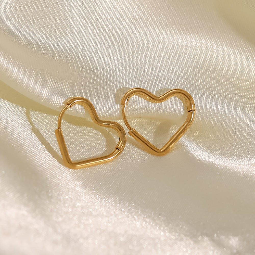The Golden pair of stainless steel heart hoop earrings propped on cream silk fabric