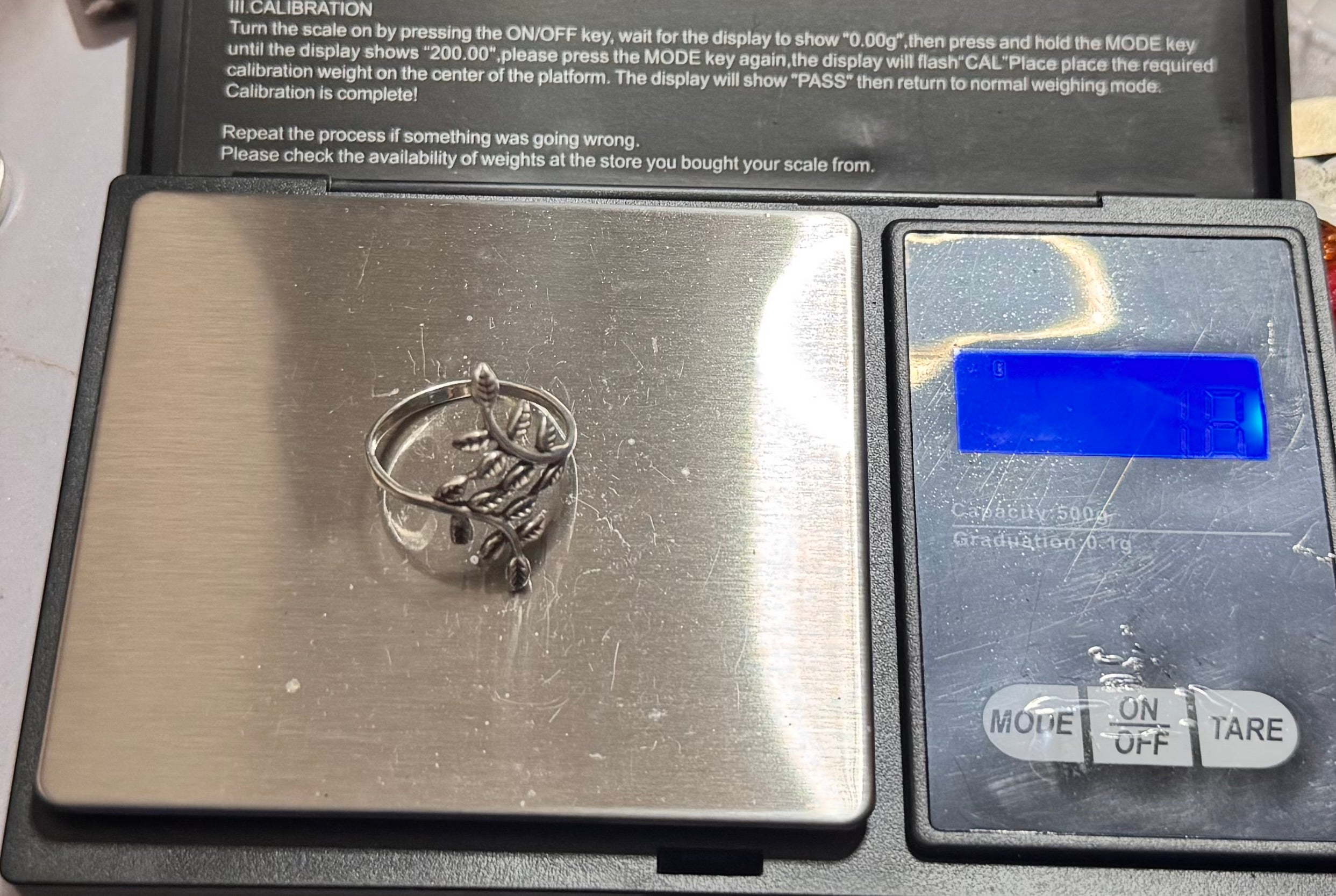 The sterling silver leaf design ring with a floral design is shown on a digital scale with a stainless steel platform and a black display unit. Its a little difficult to see but the weight is 1.8g 