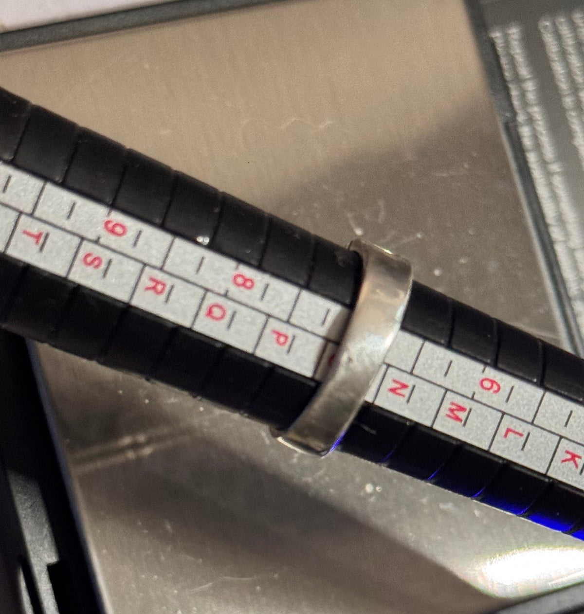 The Celtic ring on the black ring sizer with a white measurement scale printed on it, showing that the size is O