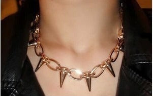 A close-up of a person wearing a spiked chain necklace with gold-toned metal spikes and links, paired with a black leather jacket.