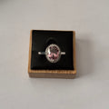 A sterling silver ring with a round pink gemstone and a halo of small clear stones, displayed in a black-lined wooden box on a light gray background. Vintage Azende Sterling Silver S925 Ring Pink Stone & Pavé