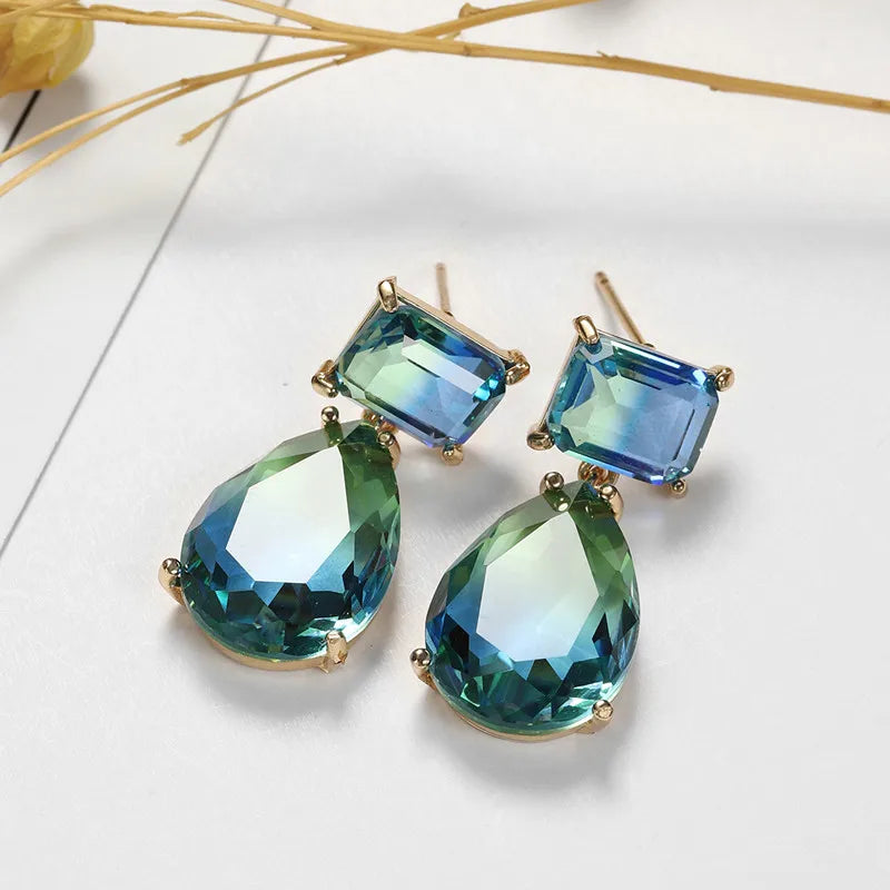 Another view of the green blue variated style laid on a white surface with the posts of the earring on show and they are a gold tone.