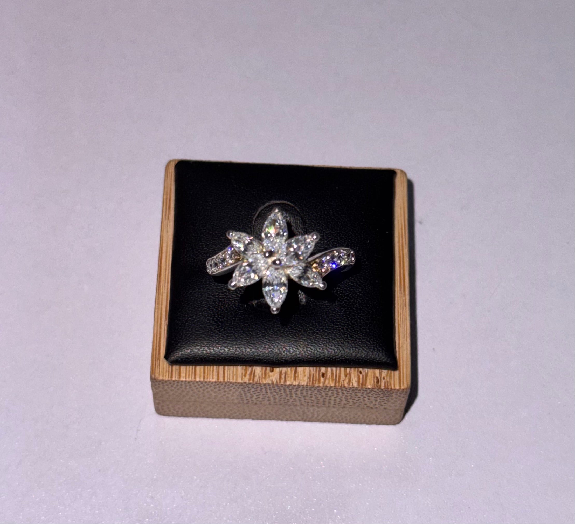 A sterling silver six-pointed starburst ring set with clear crystals, displayed on a black cushioned square jewelry box with a light wood border, set against a plain light gray background.