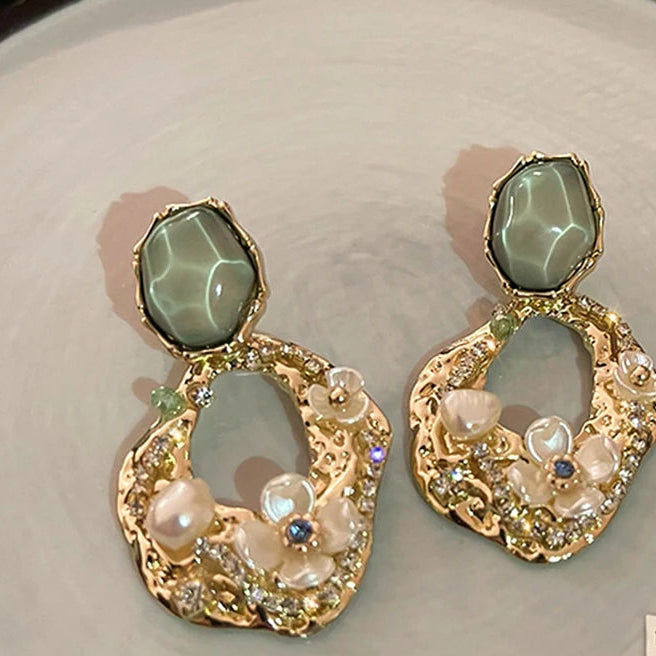 This image shows a close up of the Abstract Earrings. Absolutely stunning Earrings with gold-tone, pearls, flowers, cz's. They have a larger green stone at the studied part.