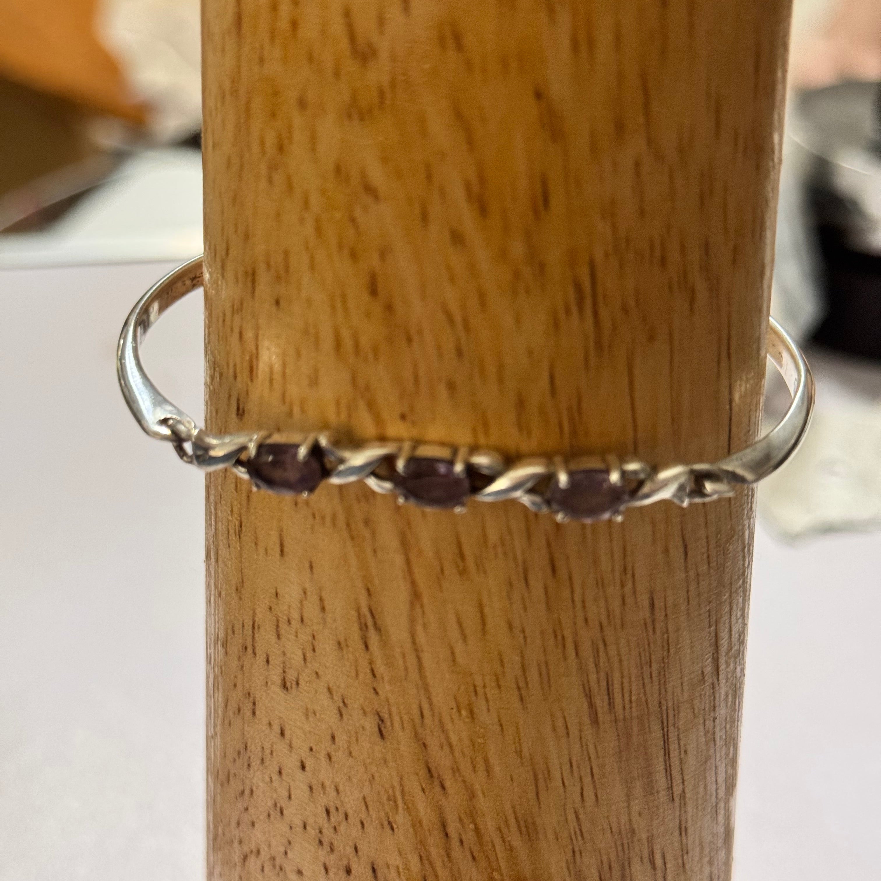 A sterling silver oval bangle style bracelet with 3 small dark purple gemstones, displayed on a wooden bracelet Mandrel