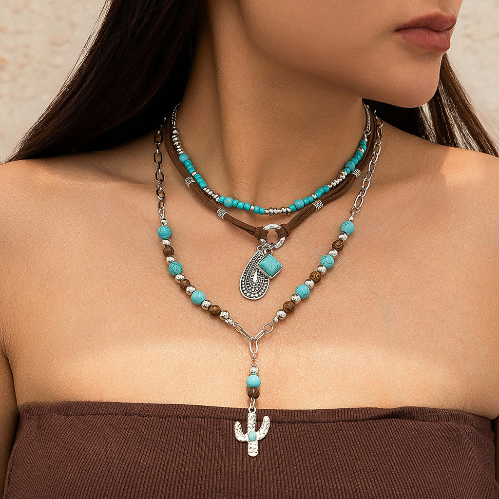 3 layers, 2 beaded necklaces one with a y style and cactus  pendant. One just varying beads in turquoise colour and silver tone. The middle necklace is suede cord joined with a metal circle with 2 pendants and abstract teardrop style pendant and a square cabochon in a bezel settng
