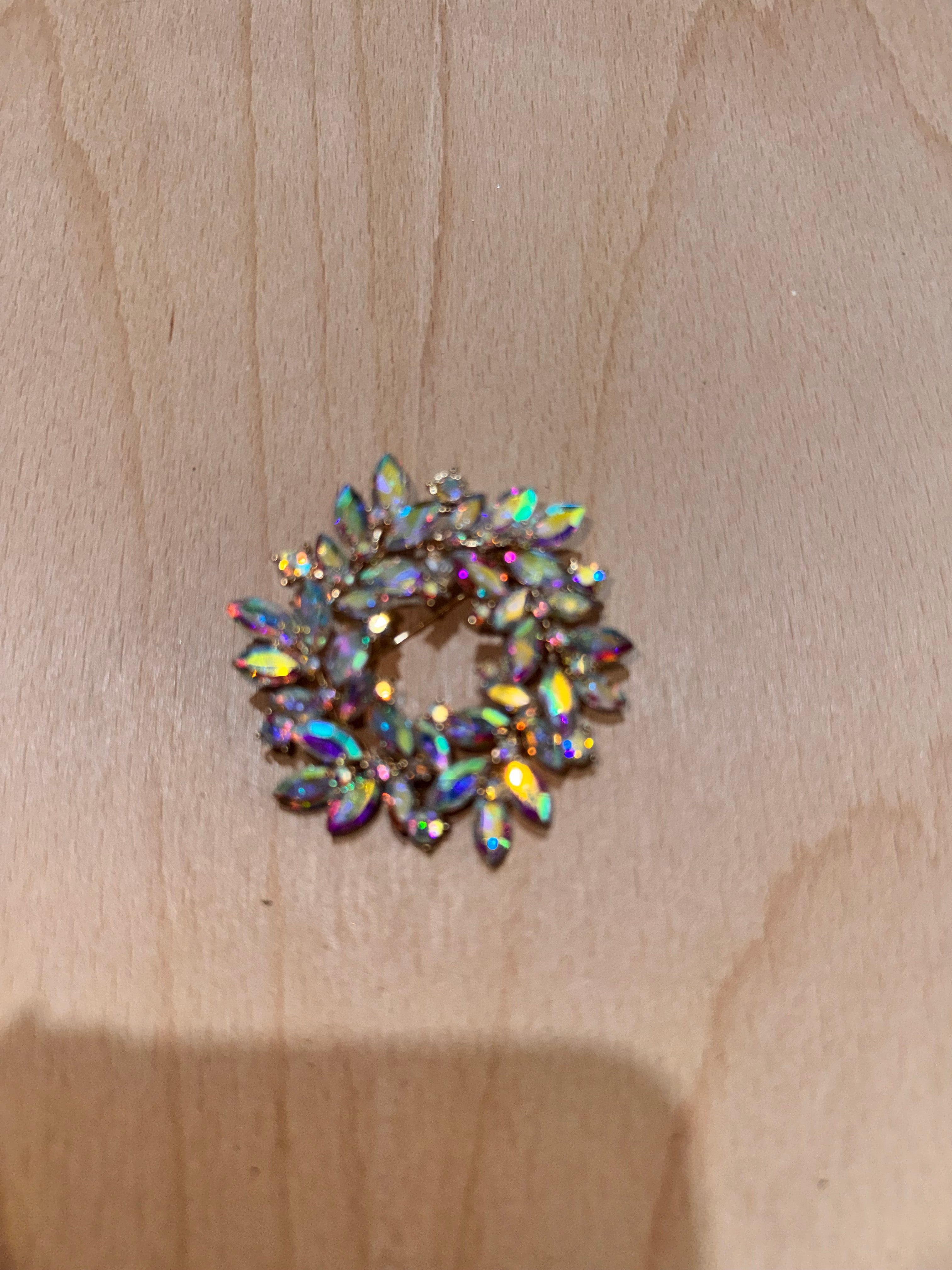 A small circular brooch with marquise-shaped iridescent rhinestones on a light wood background.