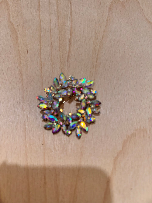 A small circular brooch with marquise-shaped iridescent rhinestones on a light wood background.