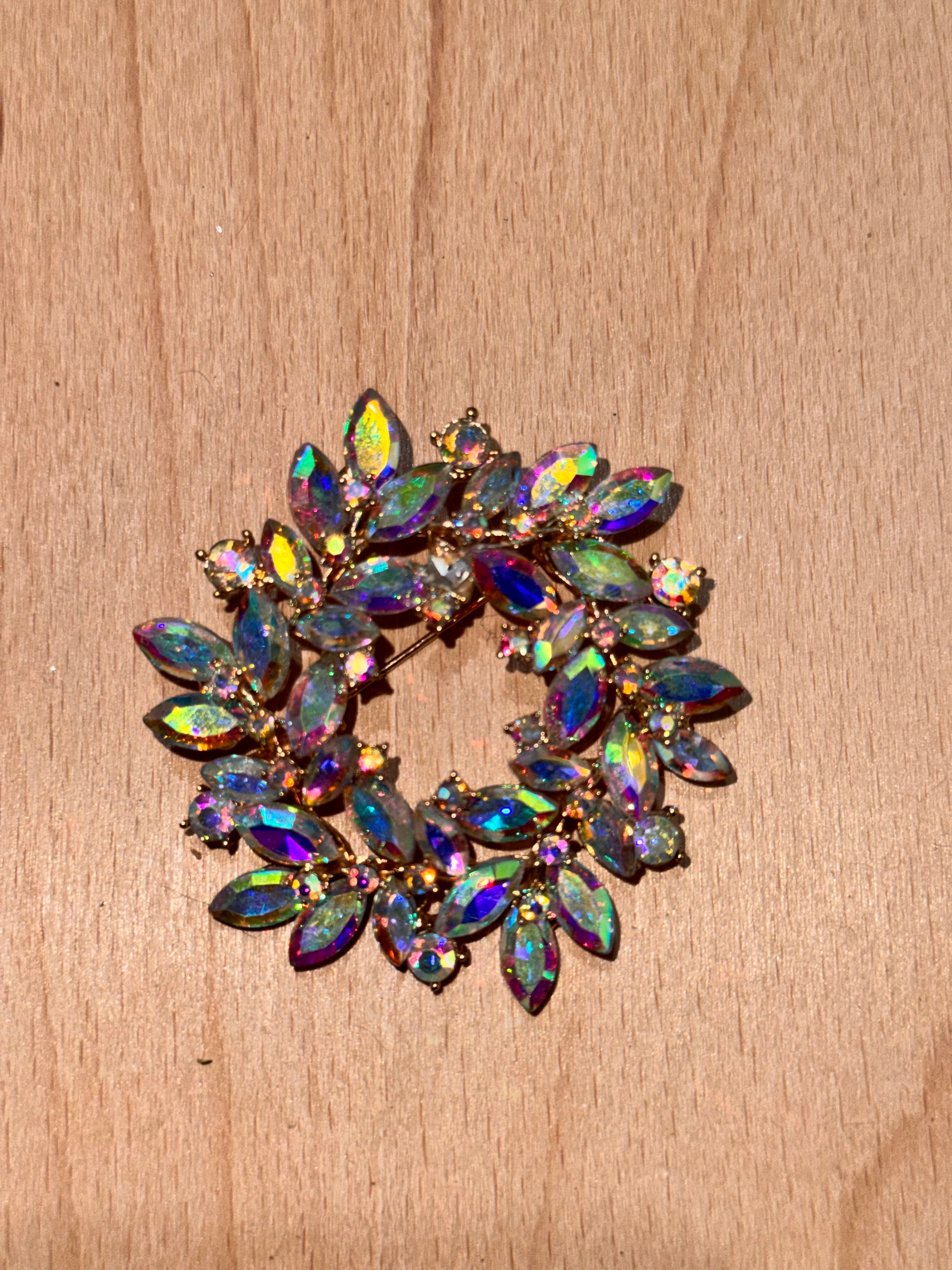 A vintage-style gold-tone brooch featuring marquise-cut iridescent rhinestones in a circular floral arrangement, displayed on a light wood surface.