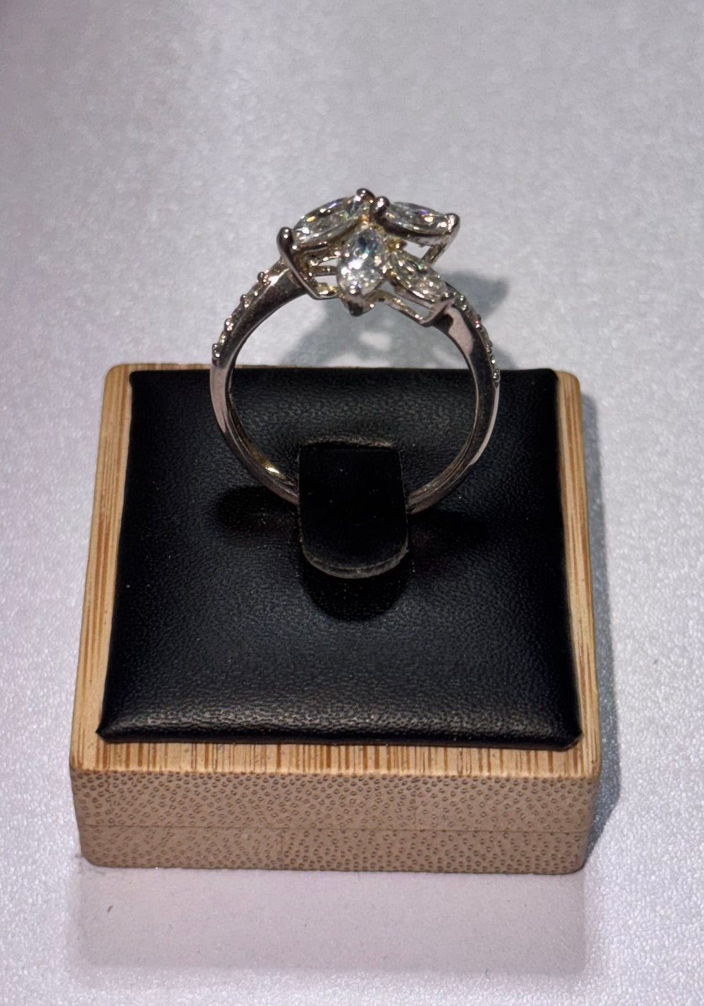 Another angle of the sterling silver ring with a starburst -shaped crystal cluster setting, displayed on a black cushion inside a light wood box