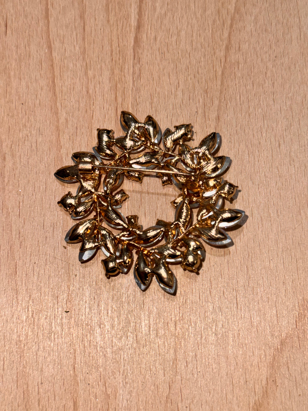 A gold-toned leafy brooch with faceted stones, photographed on the back showing pin & on a light wood surface.