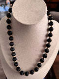 "A vintage beaded necklace with large round black satin-finish beads and small gold-toned spacer beads, displayed on a cream jewellery bust."