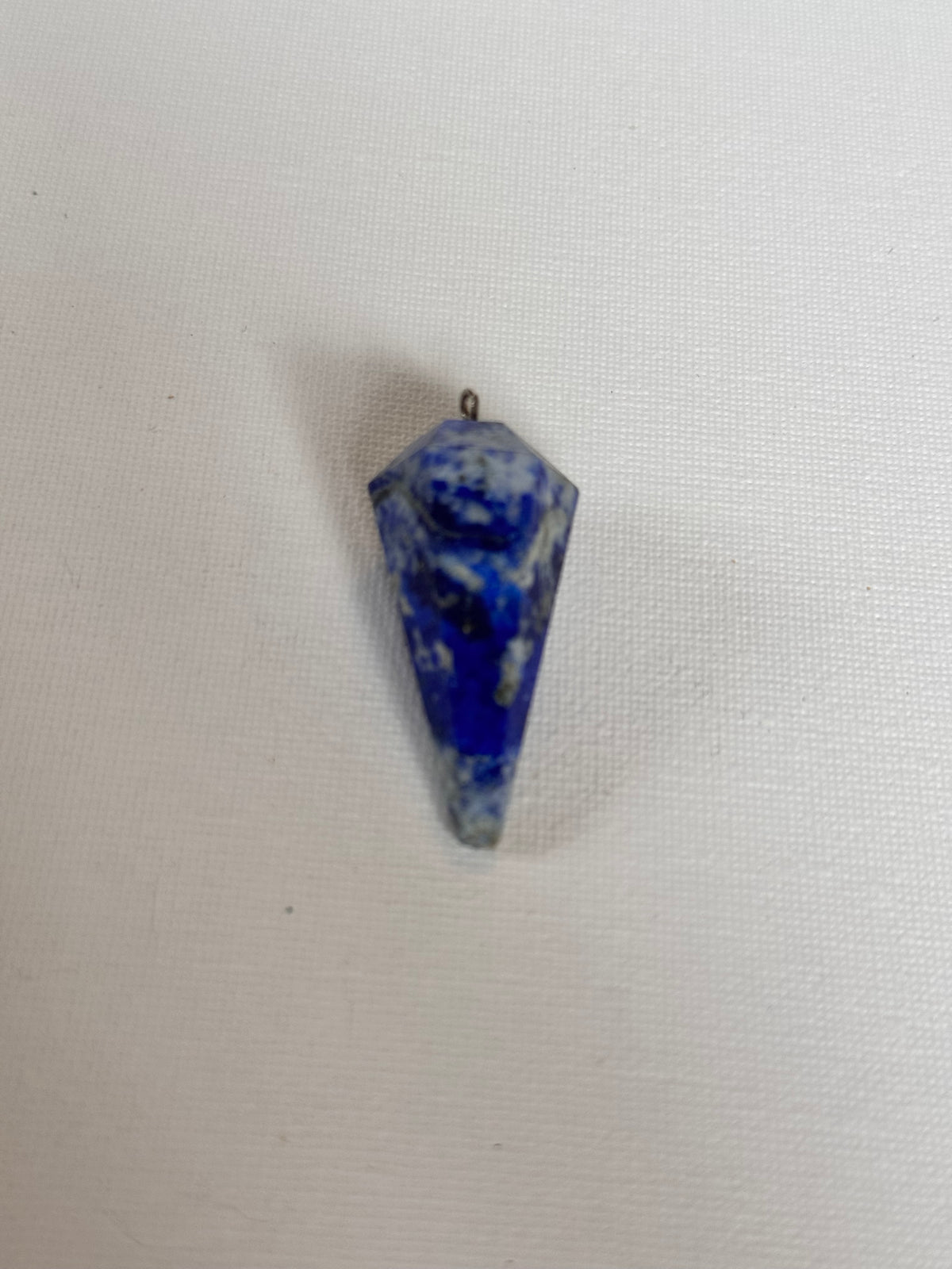 A blue and white marbled stone pendant with a small metal loop at the top, shown on a textured off-white background.