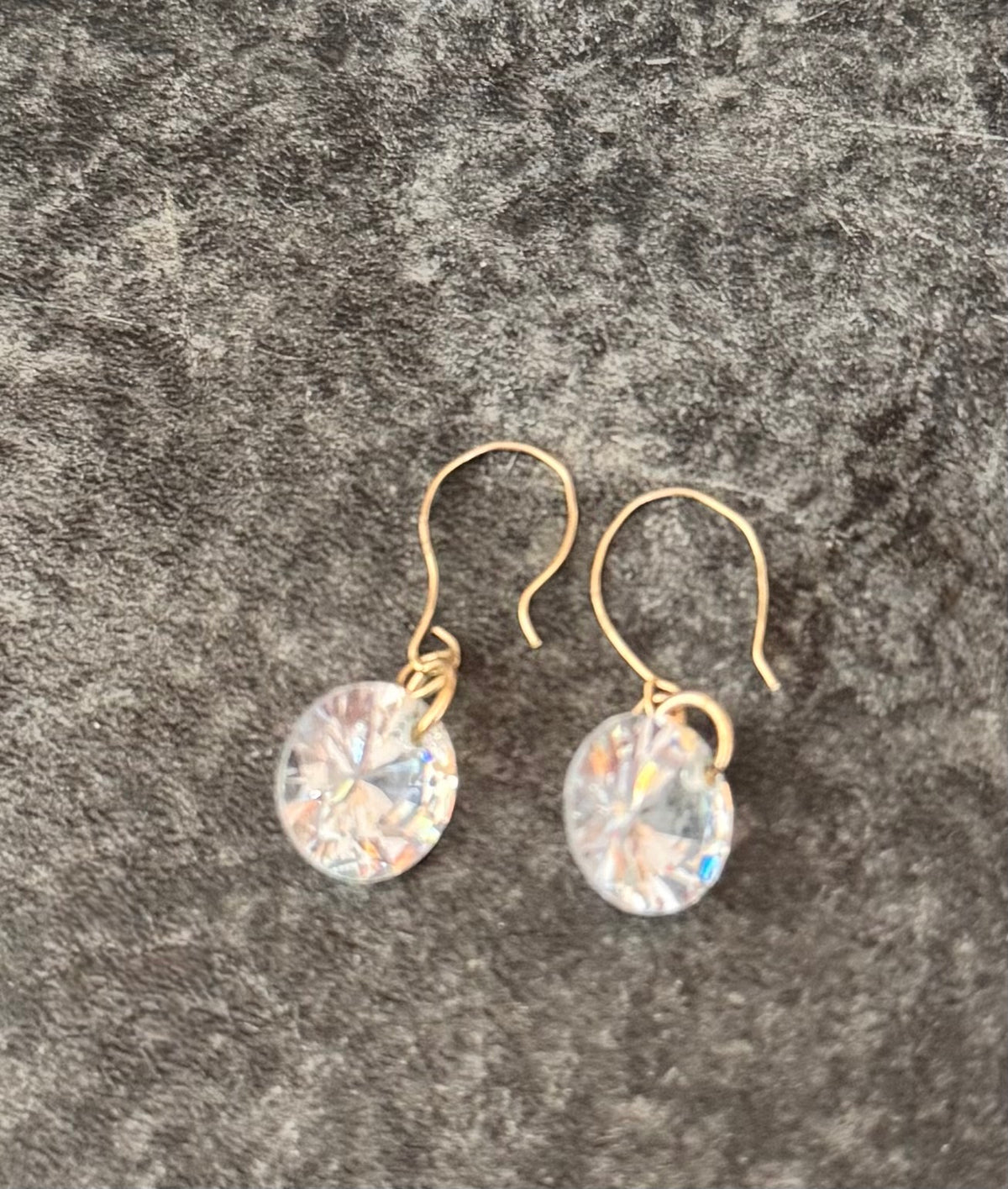A pair of 9ct Gold dangle earrings with round, faceted clear iridescent crystals, displayed on a textured gray background.