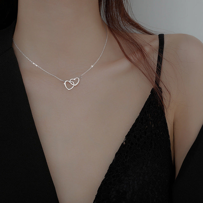 A silver-toned interlocking hearts pendant necklace. worn on a model with a black dress. English Rose