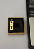 A 9 ct hallmarked 'DAD' letter pendant charm displayed on a black velvet jewelry box, next to a black and silver device, on a light gray background.