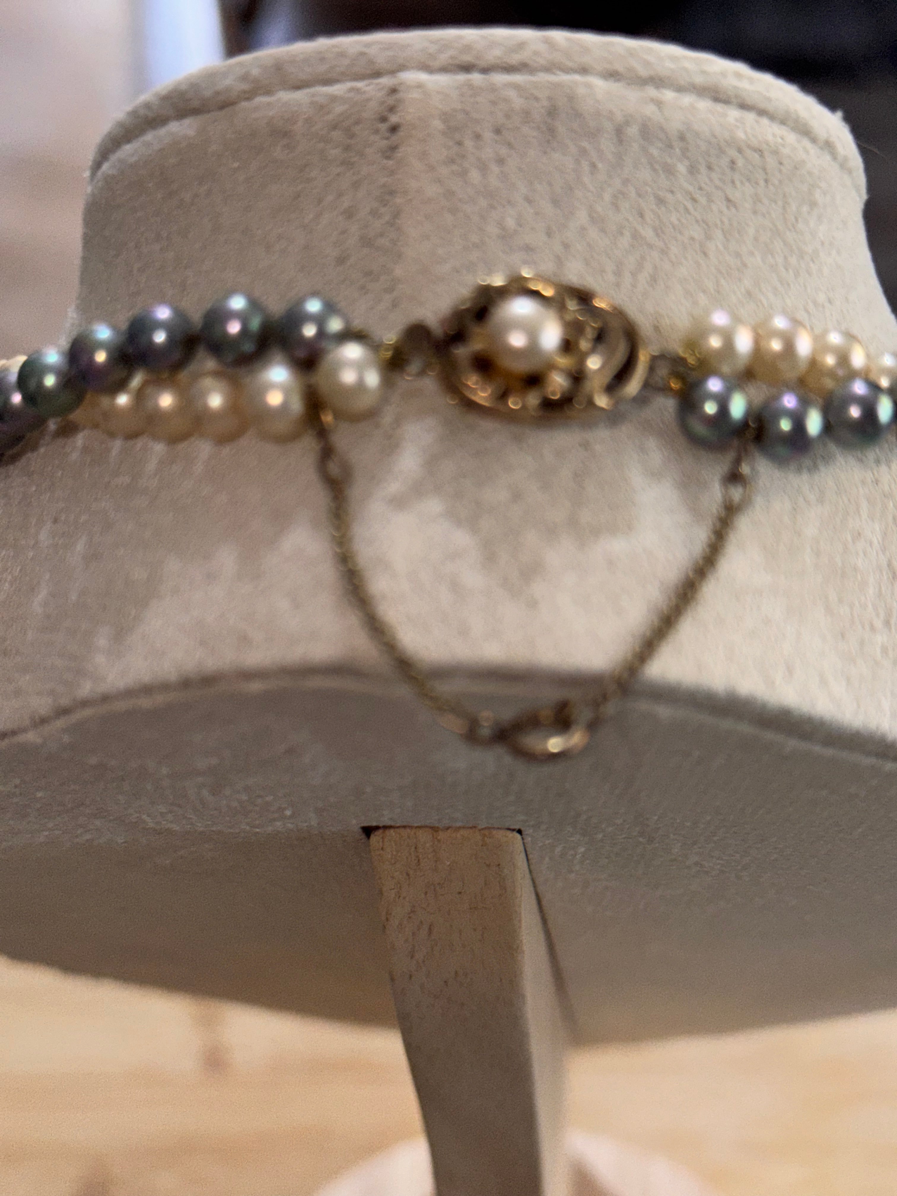 A cream & gray faux pearl double strand necklace with a vintage-style bronze filigree clasp and chain closure, displayed on a beige velvet jewelry bust.