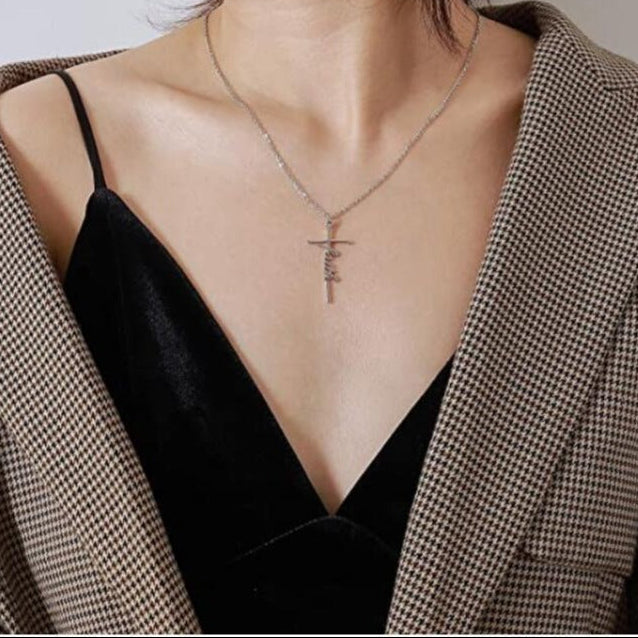 This image shows the silver style of the faith cross and chain worn against a black top and clack and white dog tooth fabric style jacket