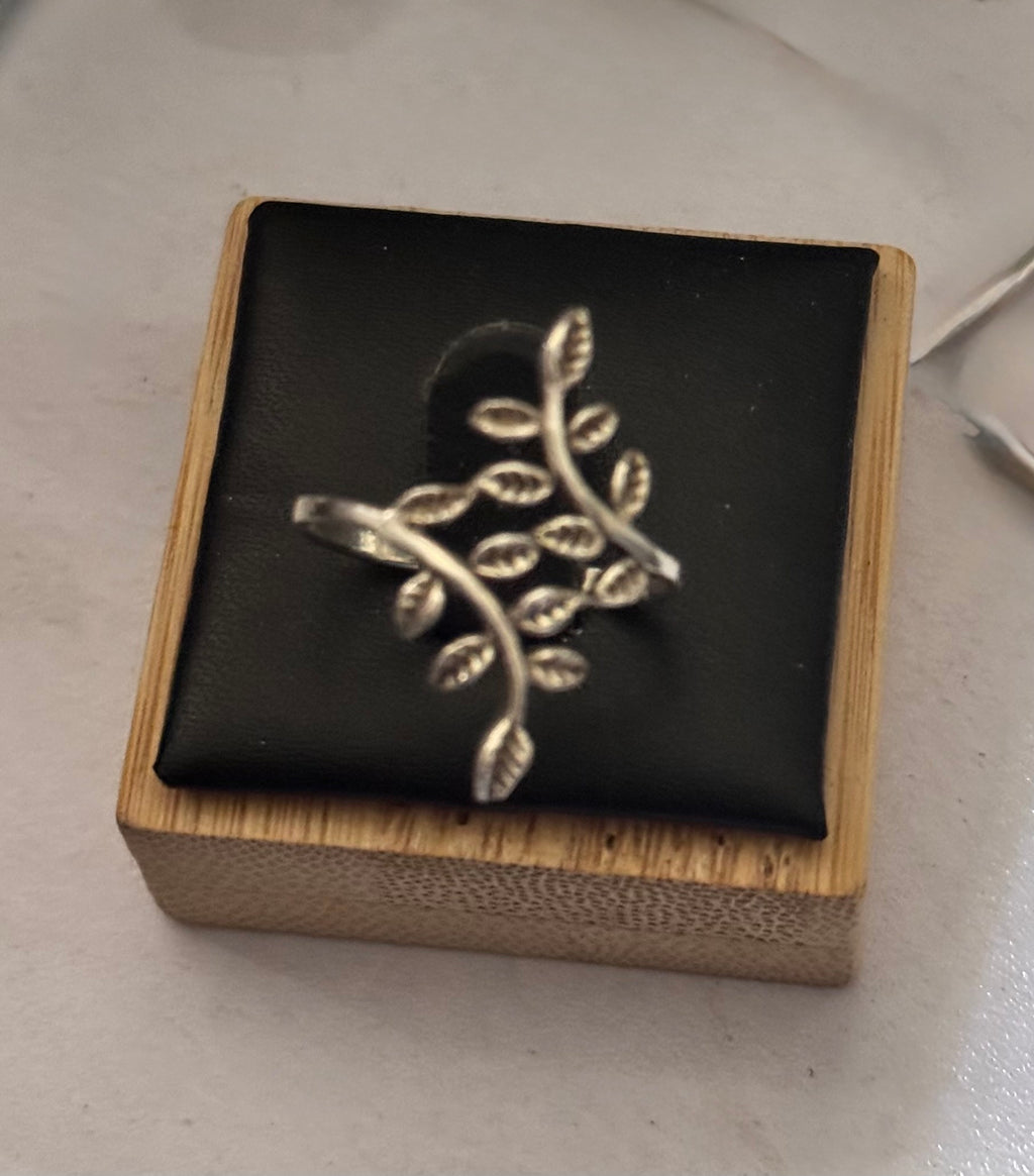 A close up of the sterling silver leaf-shaped ring displayed on a black cushion inside a small wooden box, placed on a light surface.