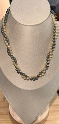 A double-strand beaded necklace with alternating dark gray and light beige pearls, displayed on a beige fabric jewelry bust.