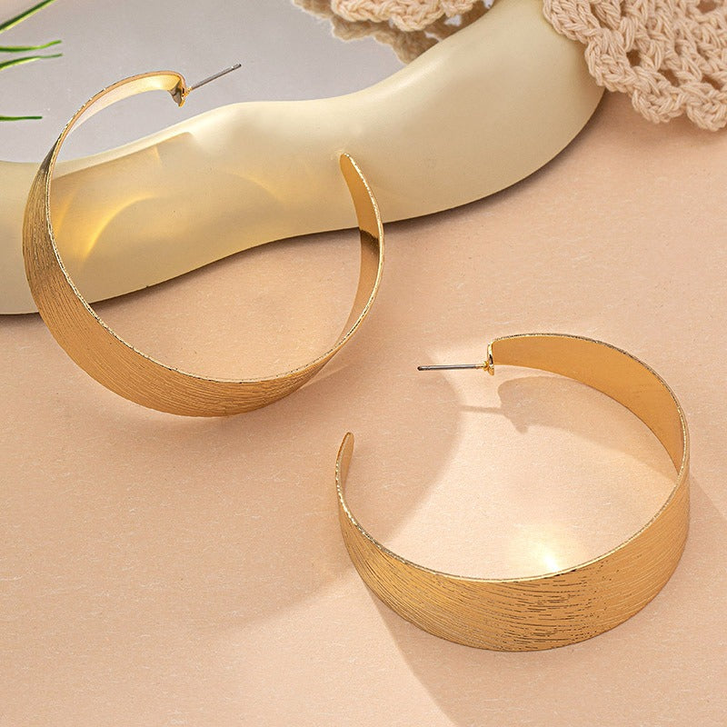 This image has the earrings laid down to show the posts. ! pair of textured half hoops. the wider style of the 80s