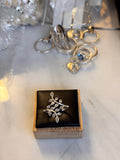 A sterling-silver ring with a leafy branch design displayed on a black cushioned square box, with other Sterling jewelry items blurred in the background on a light marble surface.