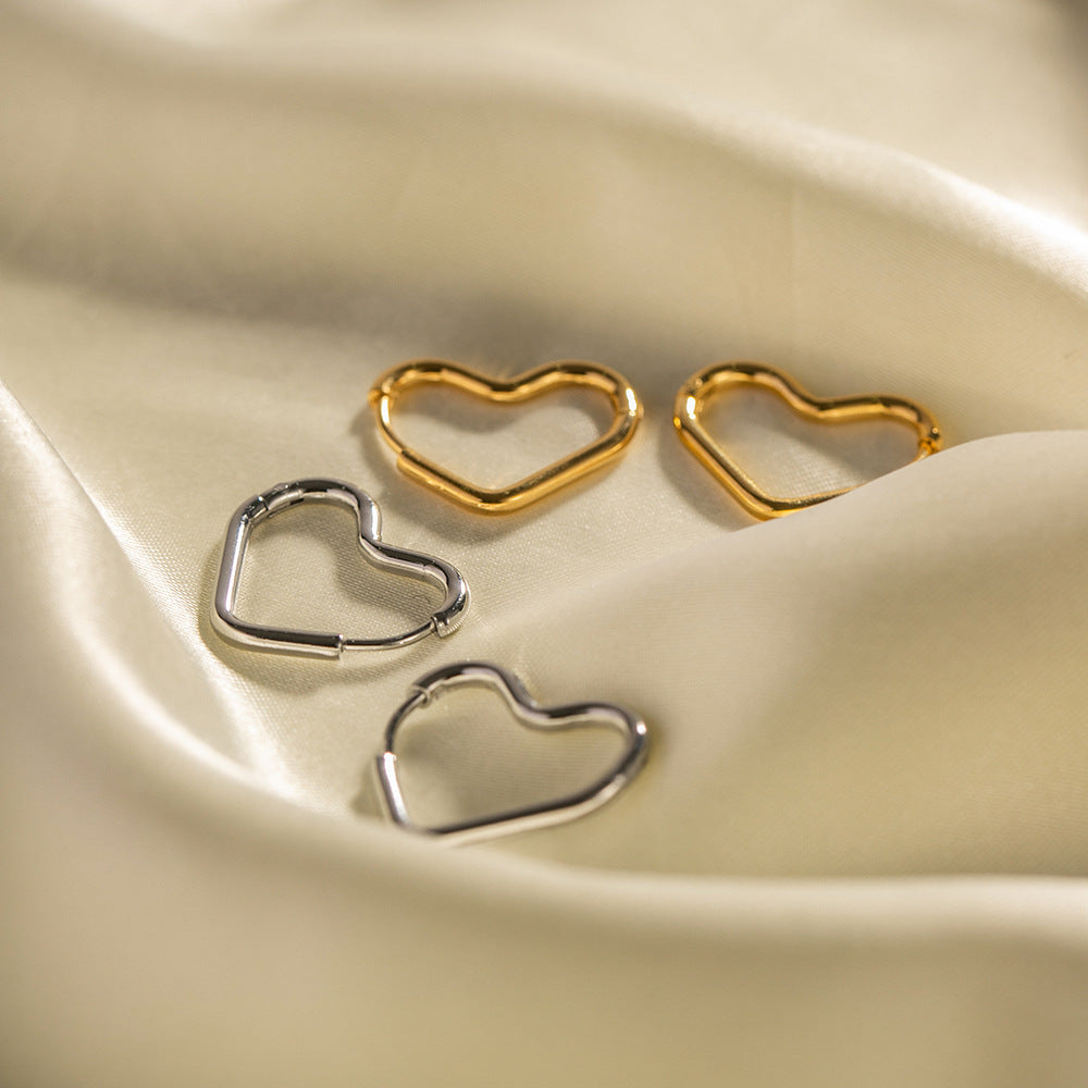 The golden hoop earrings and silver-tone stainless steel earrings in a heart shape laid on cream silk.
