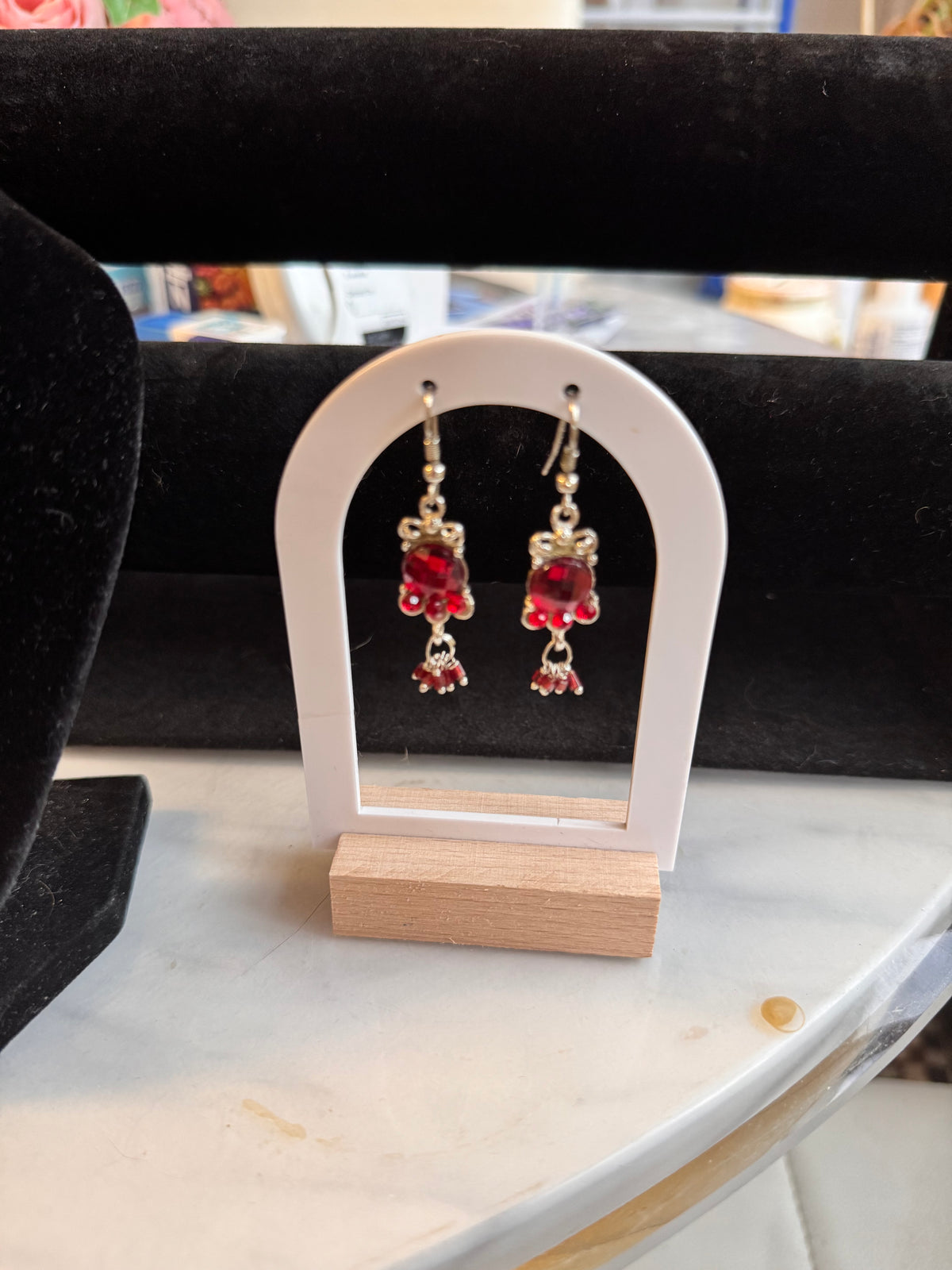 Silver tone and red stone earrings decreasing in size on a white and wooden earring stand