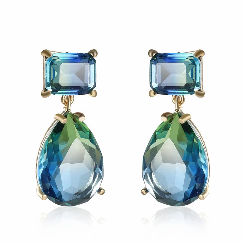 Another view of the green blue variated style laid on a white surface without the posts of the earring on display and they are a gold tone.