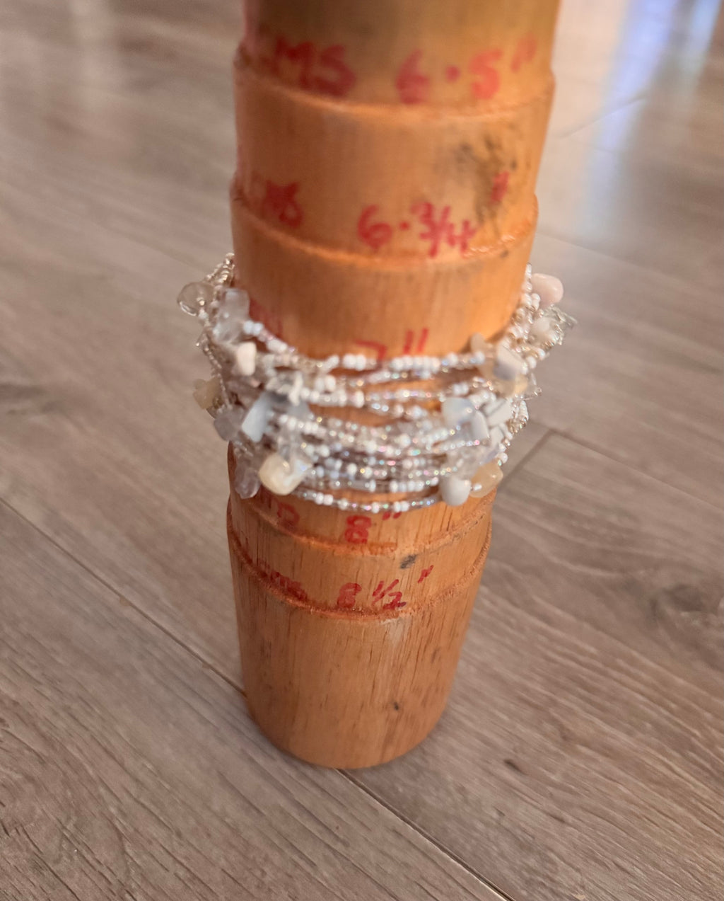 A multi-layered beaded bracelet with white, clear, and opaline beads displayed on a wooden jewelry stand on a light wood floor.