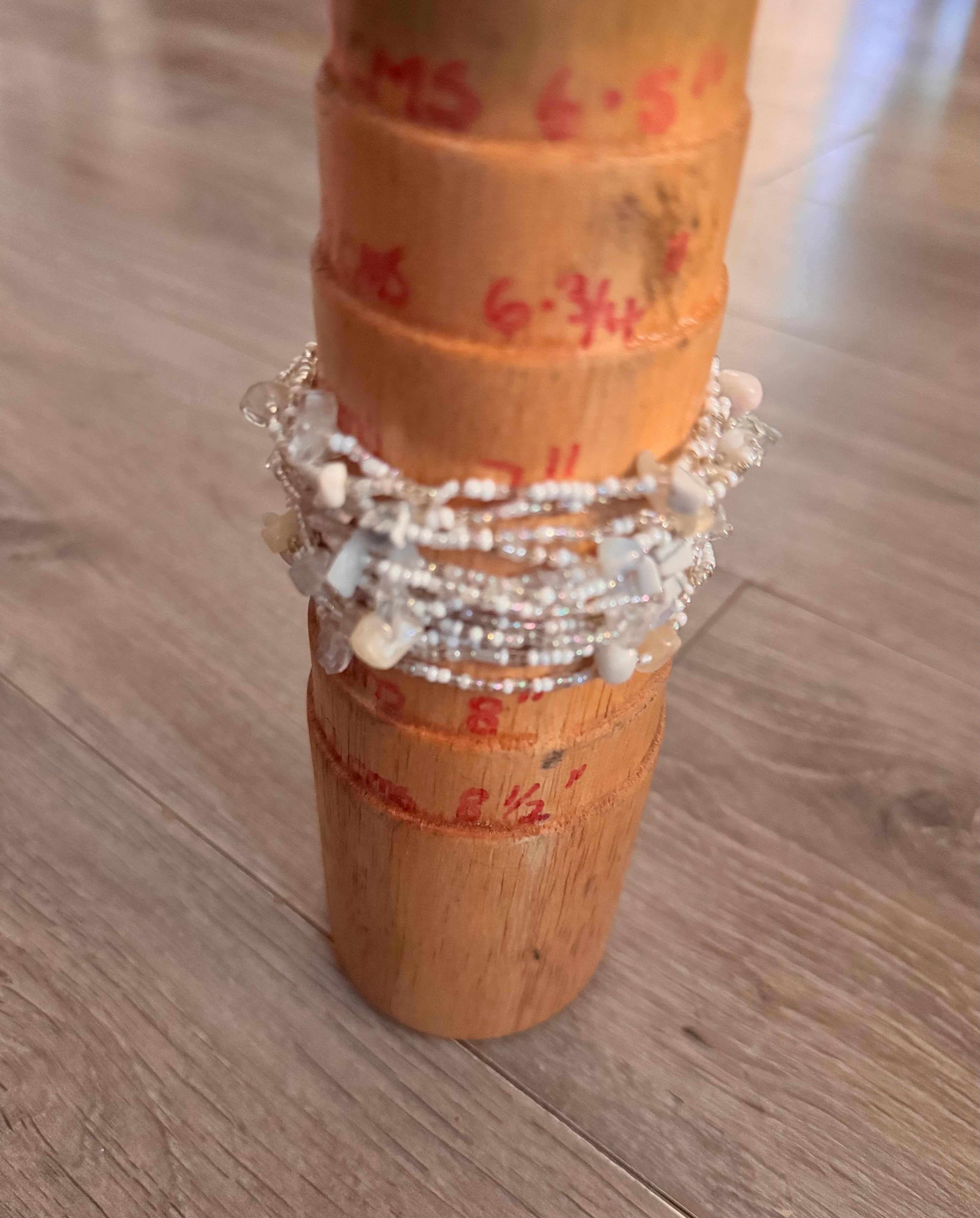 A multi-layered beaded bracelet with white, clear, and opaline beads displayed on a wooden jewelry stand on a light wood floor.