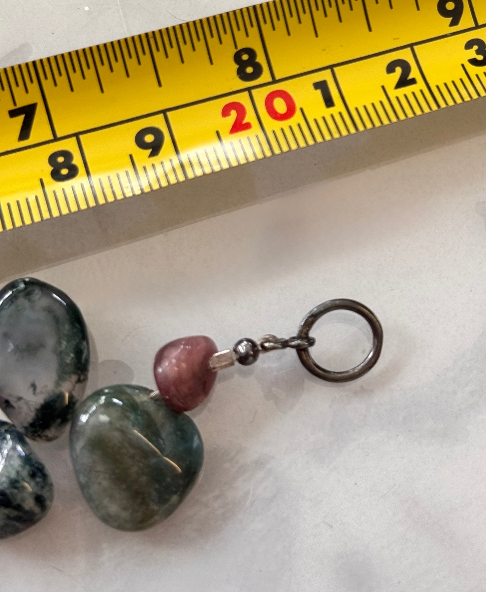A close-up of a handmade beaded bracelet with polished stones, shown next to a yellow measuring tape and other matching stones on a light surface. This image highlights a tarished silver clasp it is stamp s 925